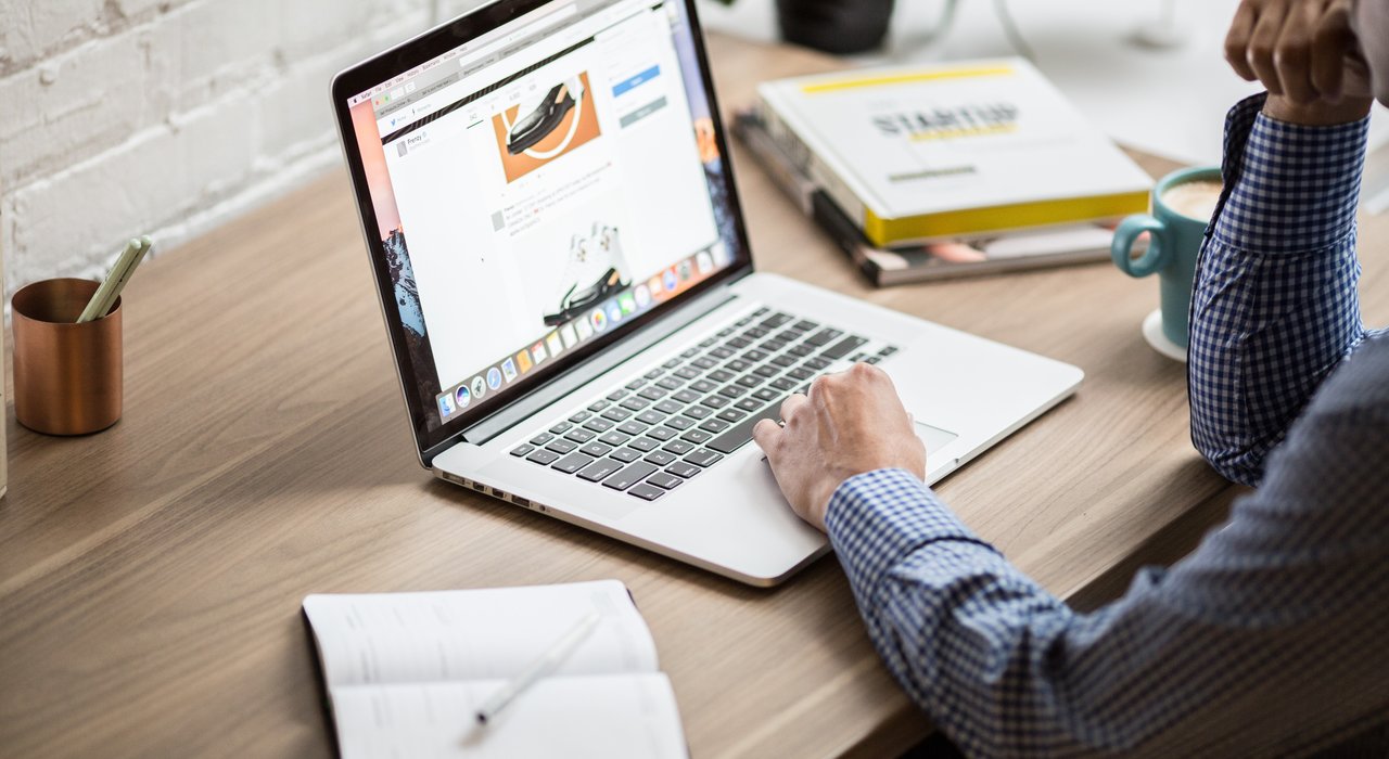 Eine Person sitzt mit Laptop und Notizbuch an einem Tisch und arbeitet.